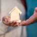 Gros plan de mains tenant une maison miniature en bois, symbolisant la propriété d'une maison et l'investissement immobilier.