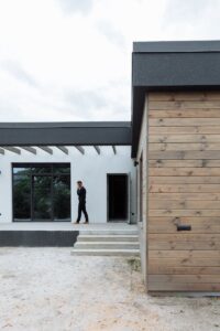 L'extérieur d'une maison moderne présente des éléments architecturaux tandis qu'un homme d'affaires parle au téléphone.
