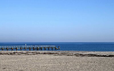 Plage sablonneuse, jetée en bois s'étendant sur la mer calme sous un ciel clair