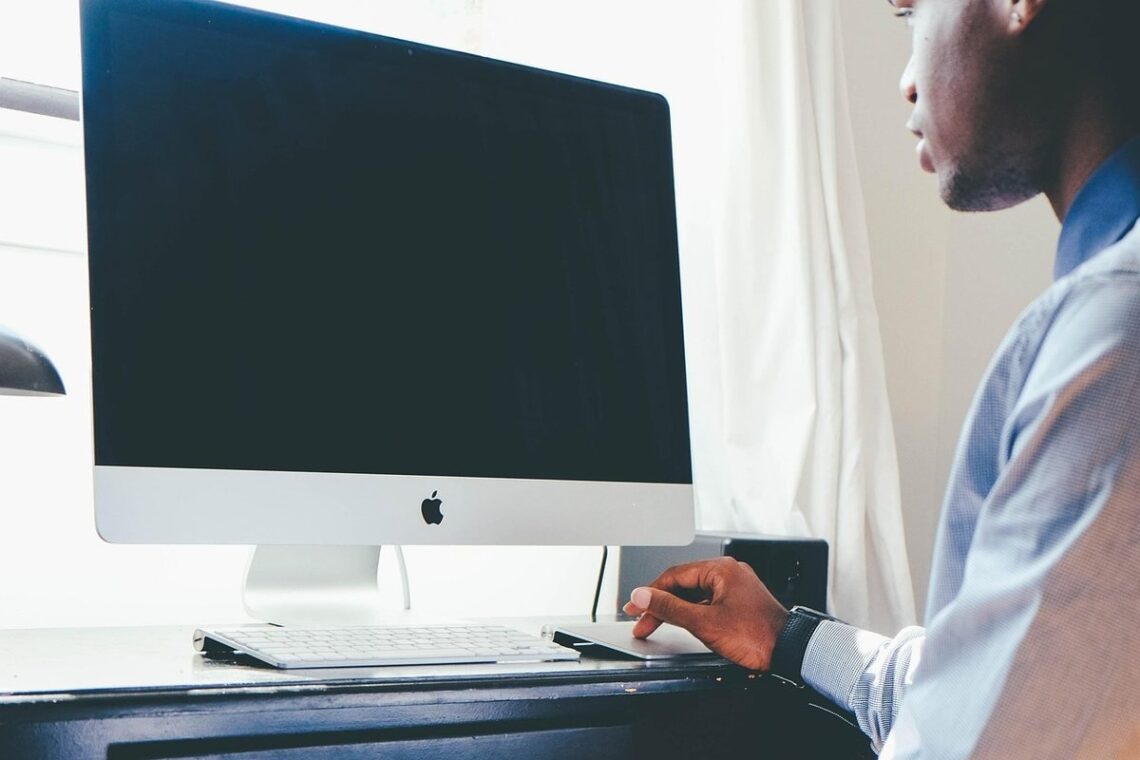 Homme assis devant un iMac, manipulant une souris, dans une pièce lumineuse