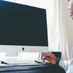 Homme assis devant un iMac, manipulant une souris, dans une pièce lumineuse