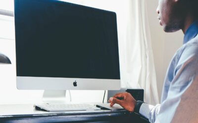 Homme assis devant un iMac, manipulant une souris, dans une pièce lumineuse