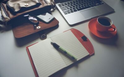 Un ordinateur portable, une tasse de café sur une soucoupe, un agenda ouvert avec un stylo, et un portefeuille sur une table